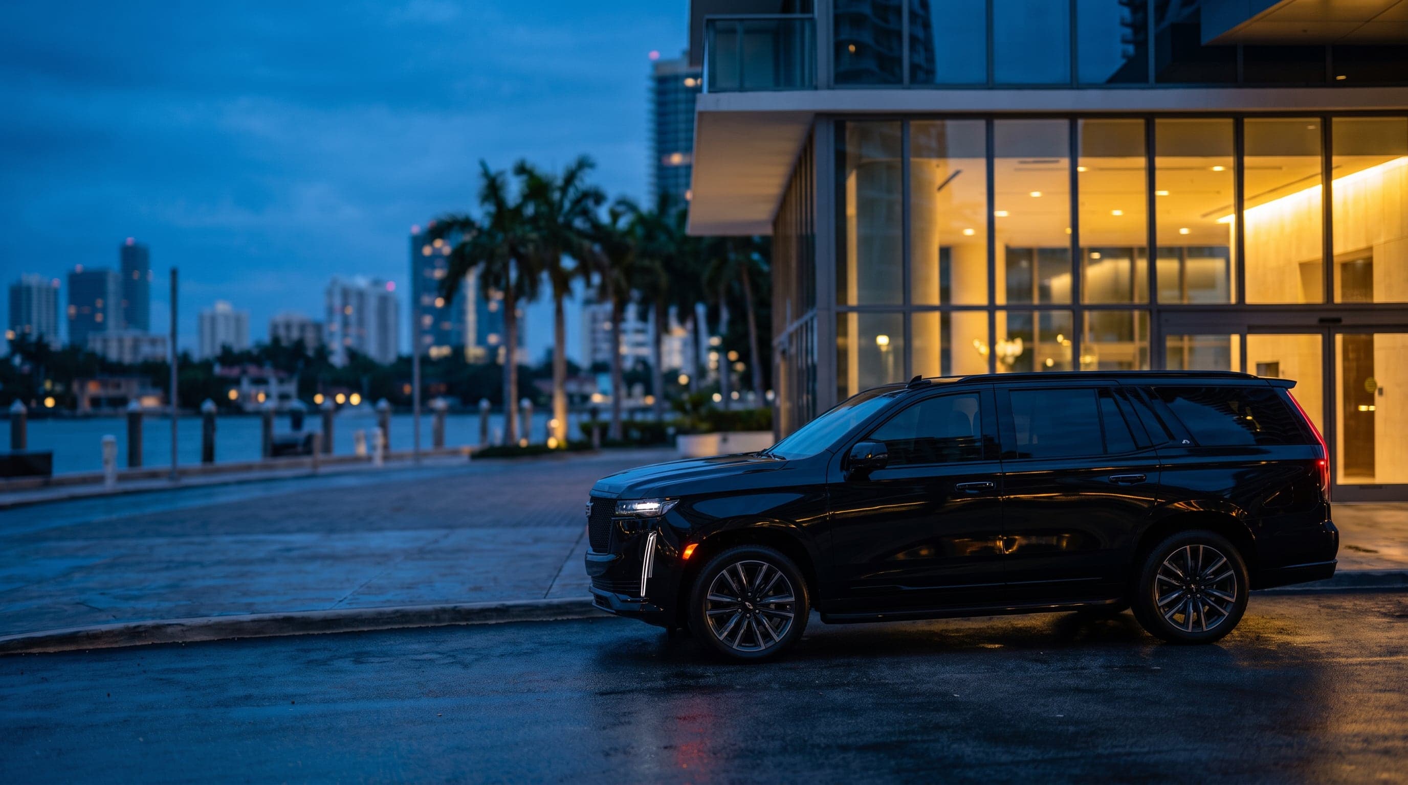 Black Cadillac Escalade ESV parked outside a glass high-rise lobby in Brickell, Miami, at blue hour